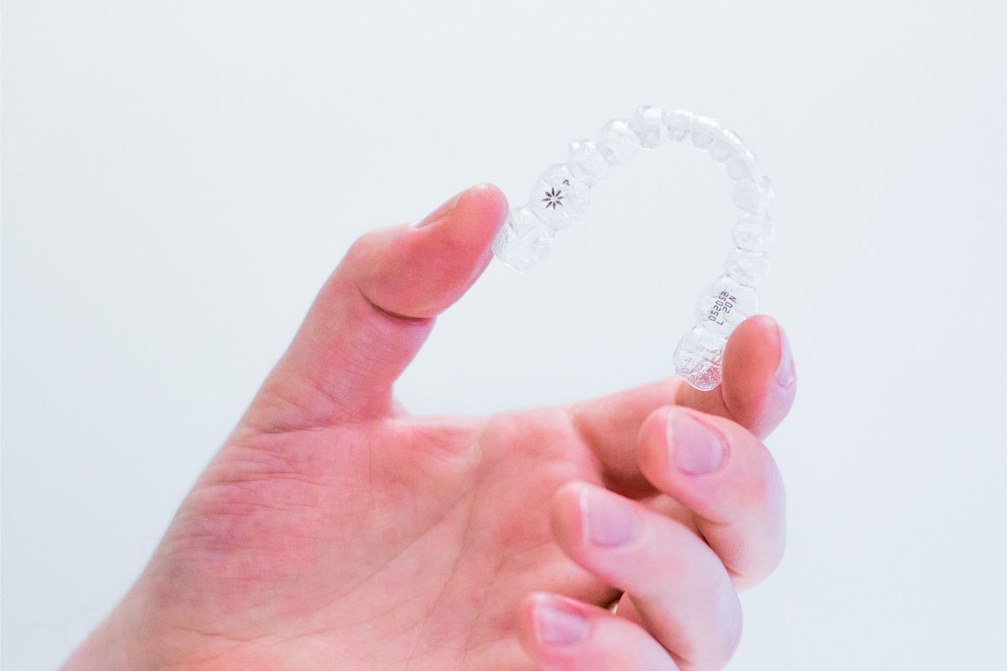 Hand holding Invisalign clear aligners for teeth straightening in Tigard, an alternative to braces from Bull Mountain Orthodontics.